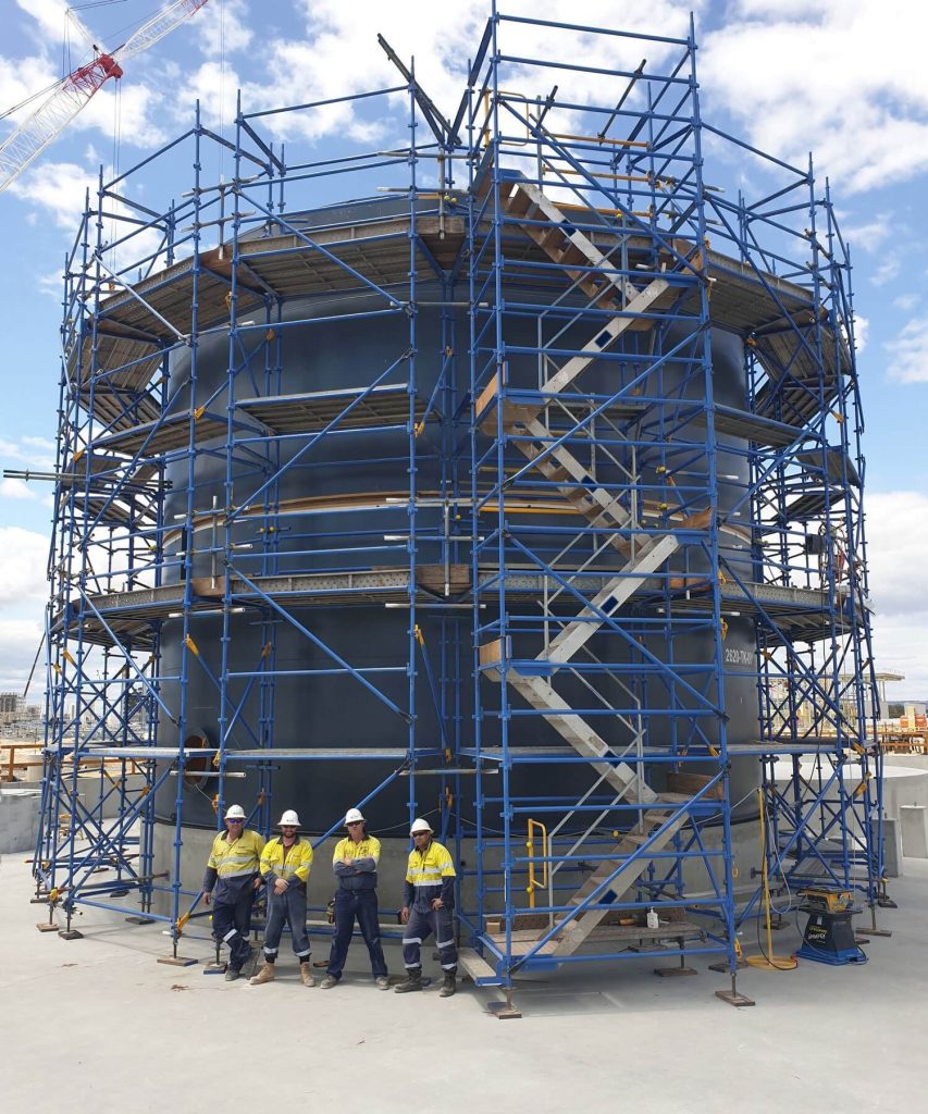 Construction team wearing safety gear and posing in front of scaffolded structure.
