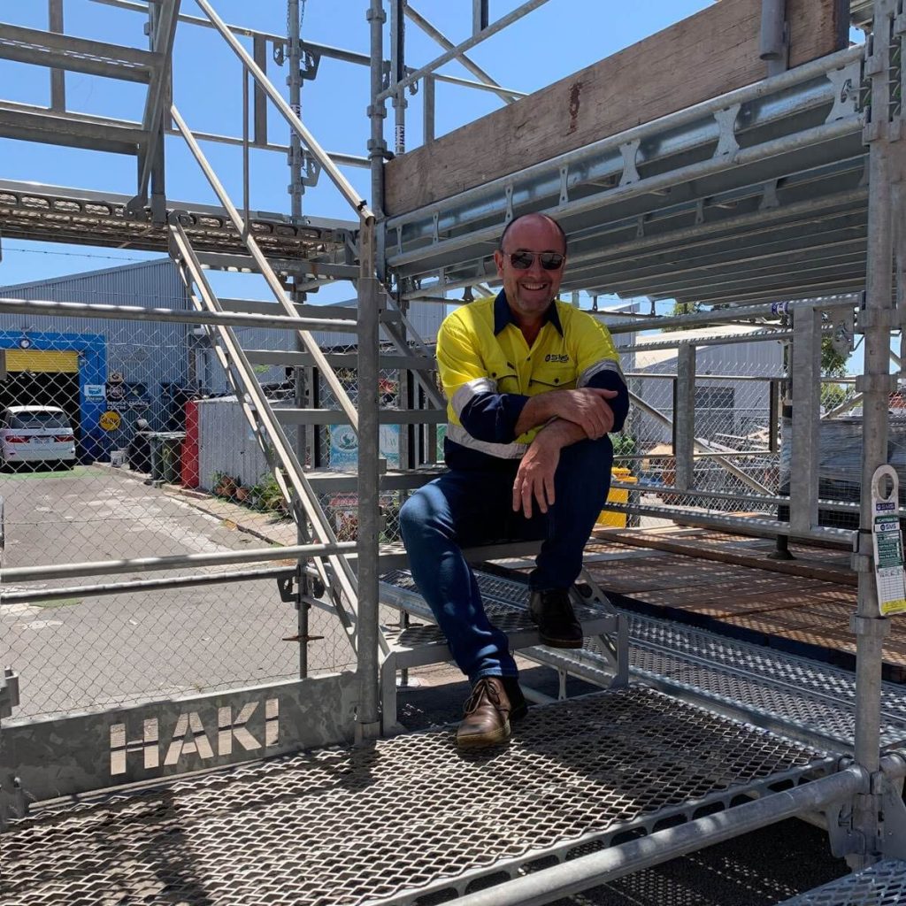 A smiling engineer sitting on a scaffold staircase.