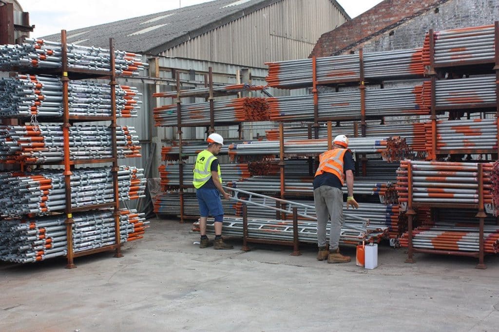 A pair of construction workers handling scaffolding material.