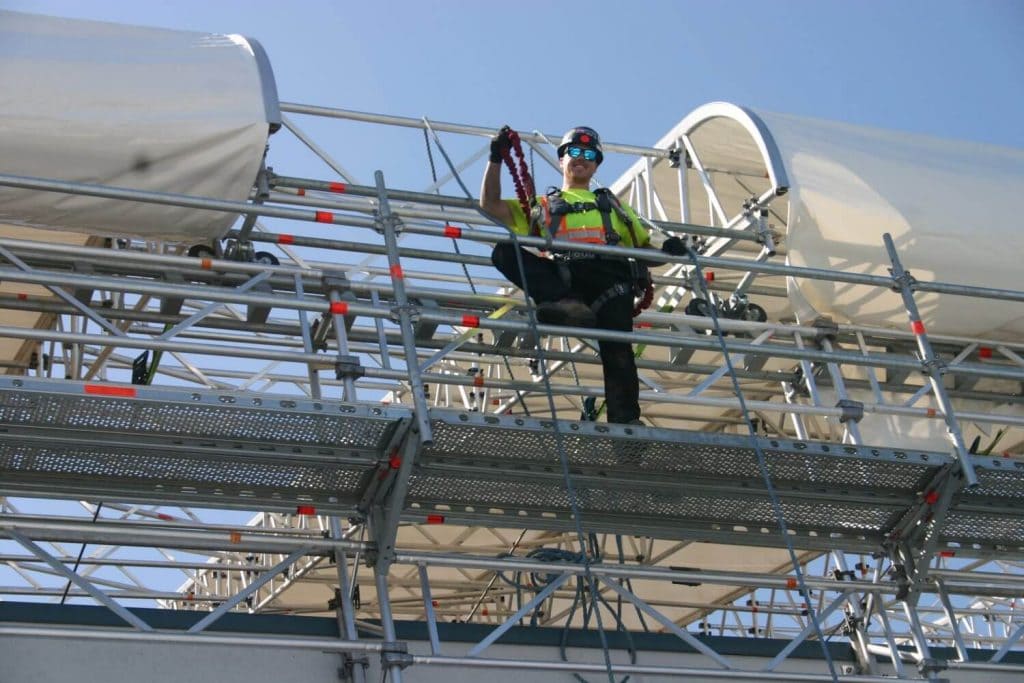 Low-angle portrait of a smiling worker standing on a scaffold at a construction site.